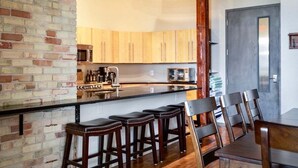 Een keuken met een bakstenen muur, houten kasten, een centraal eiland met krukken en een eethoek met stoelen.