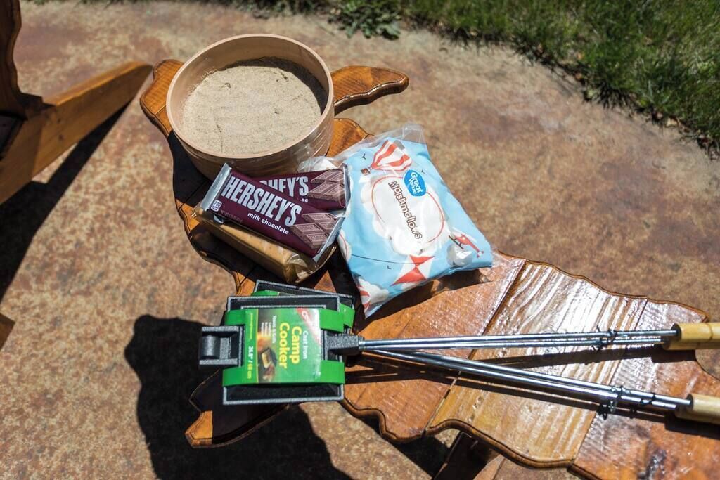 Un feu de camp avec une tablette de chocolat au lait Hershey's, un paquet de guimauves, une poêle verte pour cuisiner au feu de camp et une pince.