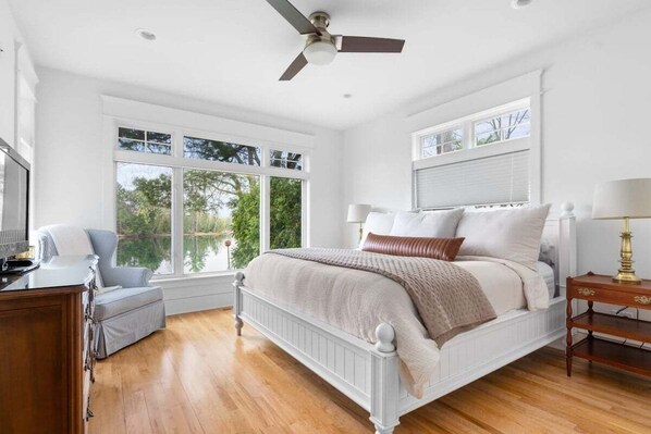 Une chambre avec un lit blanc, un bureau et une chaise. Il y a deux fenêtres et un ventilateur de plafond.