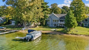 Une propriété au bord du lac, dotée d’un quai, d’une maison avec une grande pelouse et d’un bateau.