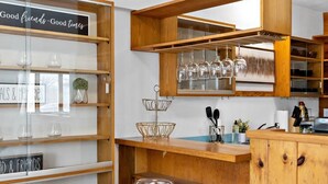 A modern kitchen with wooden cabinetry, a central island with a white table, and glass-fronted shelves displaying kitchenware.