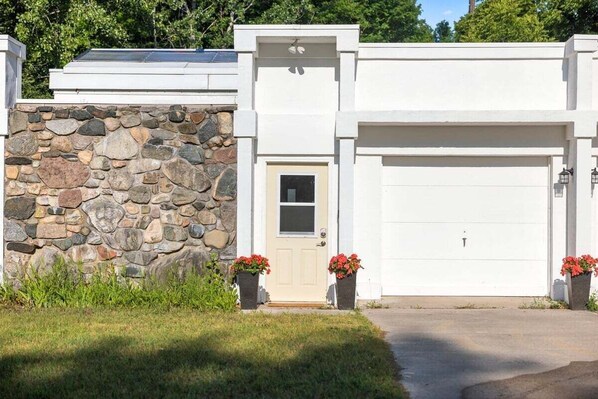 Une maison moderne avec une façade en pierre, une porte de garage blanche et une petite porte d’entrée.