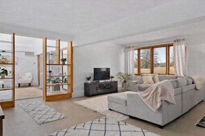 A modern living room with a grey sofa, a TV on a cabinet, and a large window with curtains.