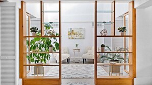 A room with a central glass partition, wooden shelving units on either side, and a small table with chairs in the middle.