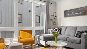 Ein modernes Wohnzimmer mit einem grauen Sofa, einem gelben Sessel und einem kleinen runden Tisch mit Blumen in einer Vase.
