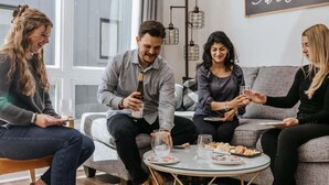 Eine Gruppe von Personen sitzt auf einer Couch und einem runden Tisch mit Tellern und Gläsern.