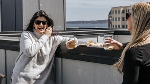 Zwei Personen auf einem Balkon mit schöner Aussicht auf ein Gewässer und Gebäude im Hintergrund.