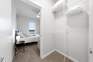 Ein Hotelzimmer mit einem Bett, einem Nachttisch mit Lampe, einem Fenster mit Ausblick und einem begehbaren Kleiderschrank mit Kleidung.