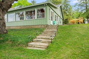 A green house with a front porch, a set of stone steps, and outdoor furniture.