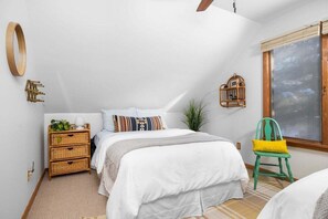 A bedroom with a bed, a nightstand, a green chair, a window, and a wall-mounted birdcage.