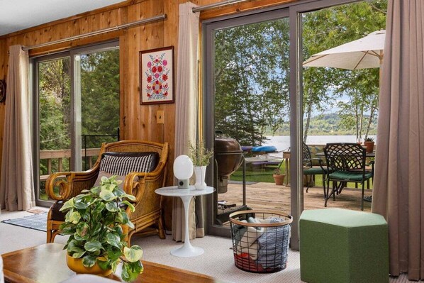 A room with large sliding glass doors to a deck, wicker furniture, a small white table, and a green ottoman.