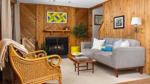 A cozy living room with a fireplace, a sofa, a wicker chair, and a coffee table. - Camp Birch: Waterfront Home on Lake Leelanau (Lake Leelanau)