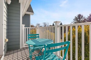 Een overdekt terras met een tafel en stoelen, een witte balustrade, en in de achtergrond bomen en een elektriciteitsleiding.