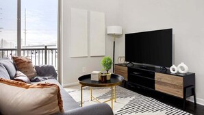 Una sala moderna con un sofá, una mesa redonda de centro, un televisor y una lámpara.