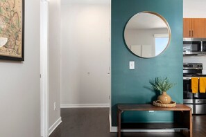 Une cuisine moderne dotée d’appareils électroménagers en acier inoxydable, d’un mur d’accent de couleur turquoise et d’un miroir rond placé au-dessus d’une petite table en bois sur laquelle se trouve une plante.