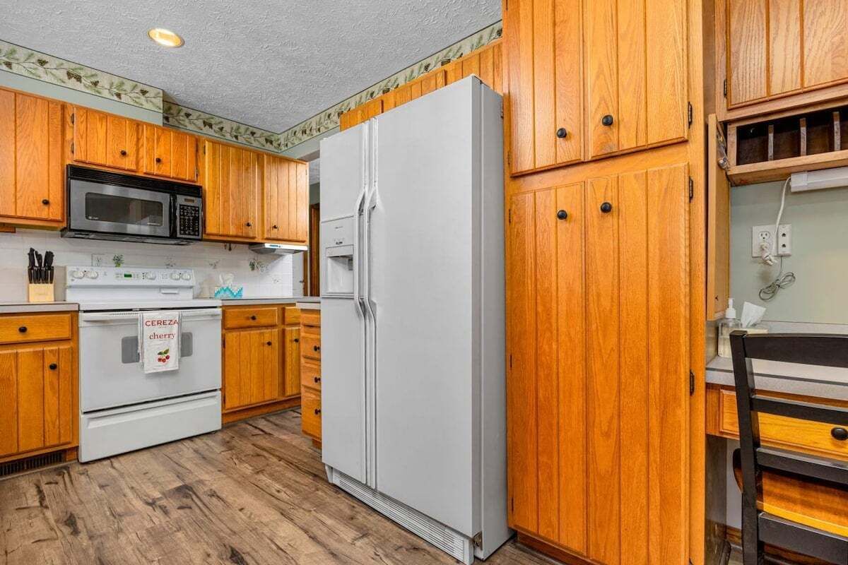 Une cuisine avec des meubles de rangement en bois, un réfrigérateur blanc, un four à micro-ondes et une cuisinière.