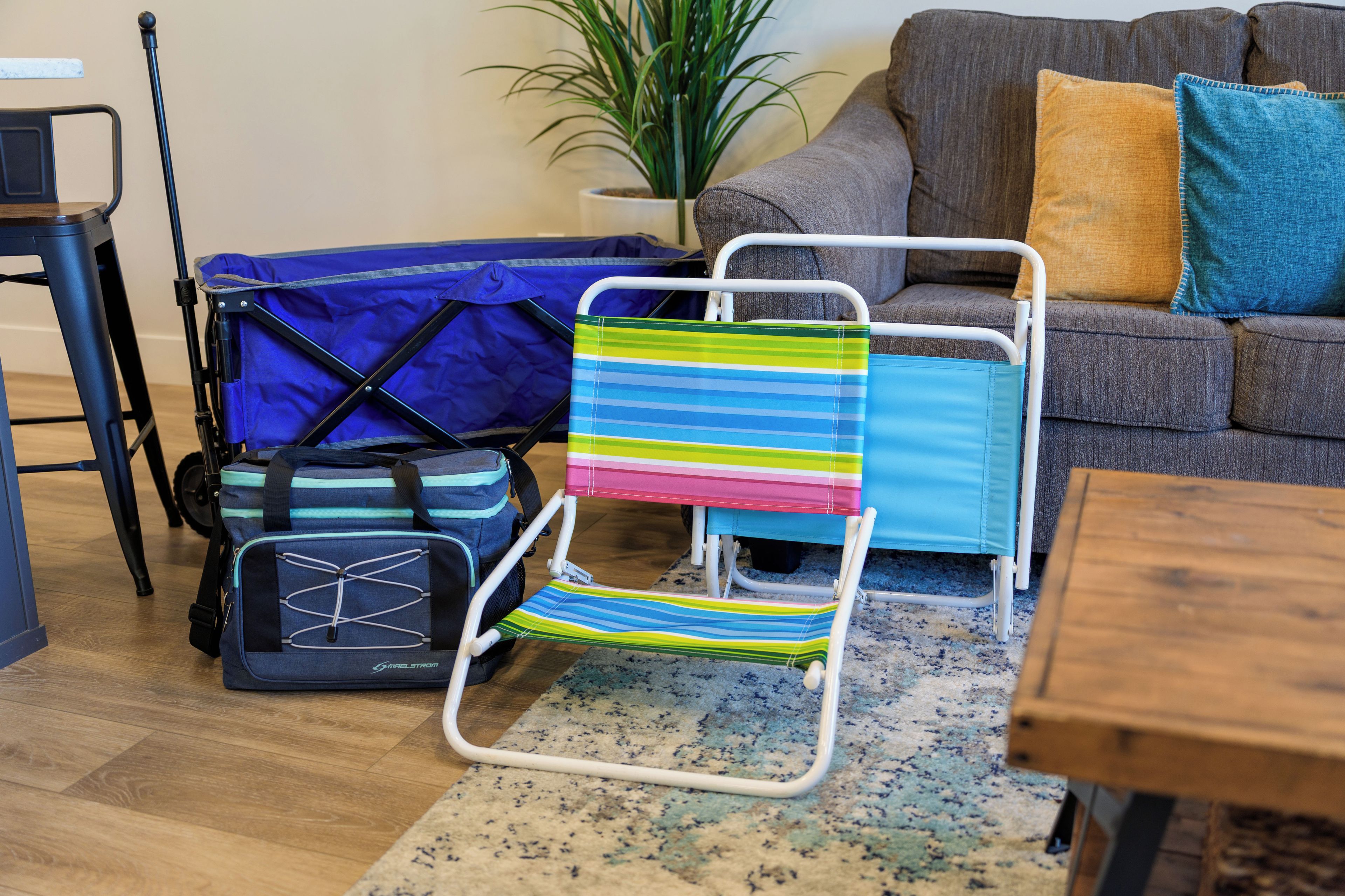 Een kamer met een opklapbare stoel, een blauw- en groen gestreepte tas, een grijze bank en een houten bijzettafeltje.