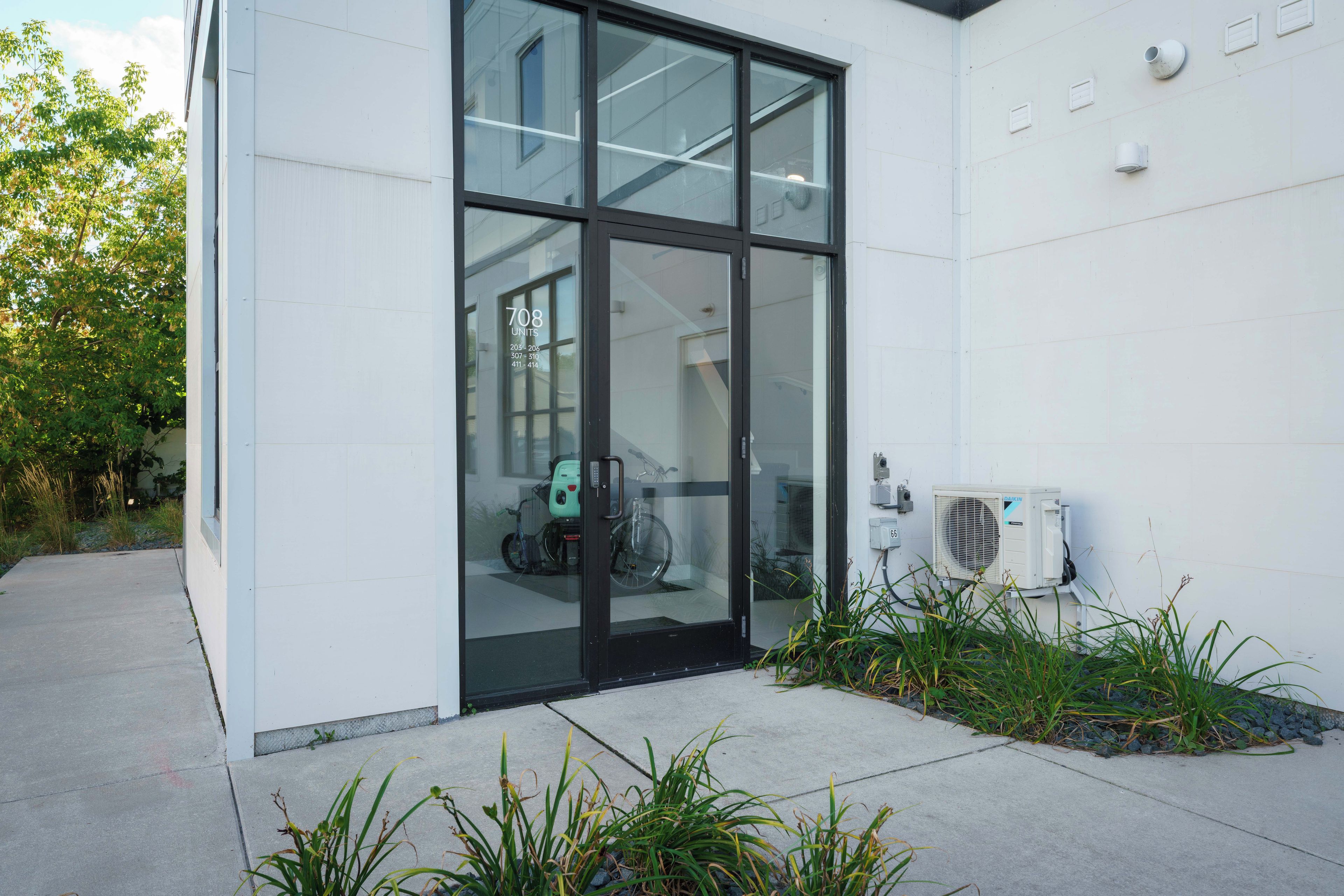 A modern building with a glass entrance, a bicycle parked inside, and an air conditioning unit on the exterior wall.