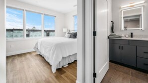 Un dormitorio con una cama grande, un baño con tocador moderno y vistas al exterior por la ventana.