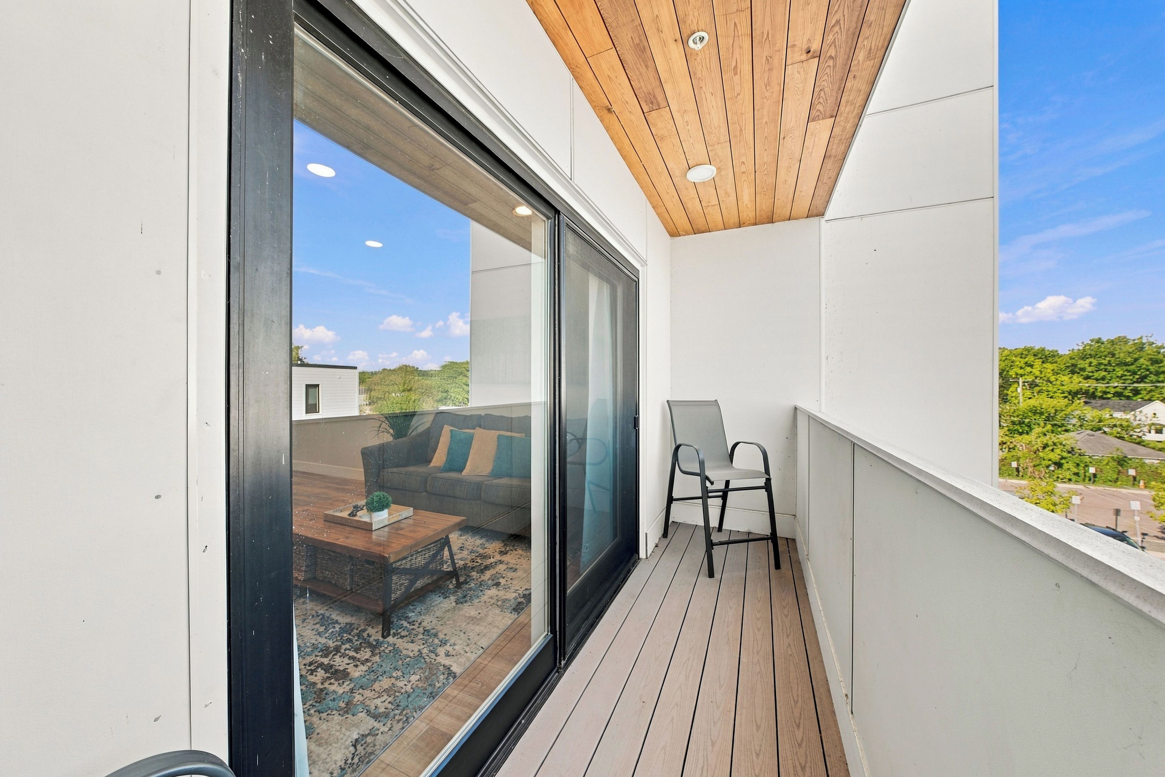 En balkon med træloft, skydedør i glas, et lille bord og en stol.
