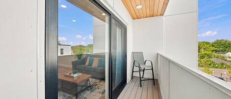 A balcony with a wooden ceiling, a sliding glass door, a small table, and a chair.