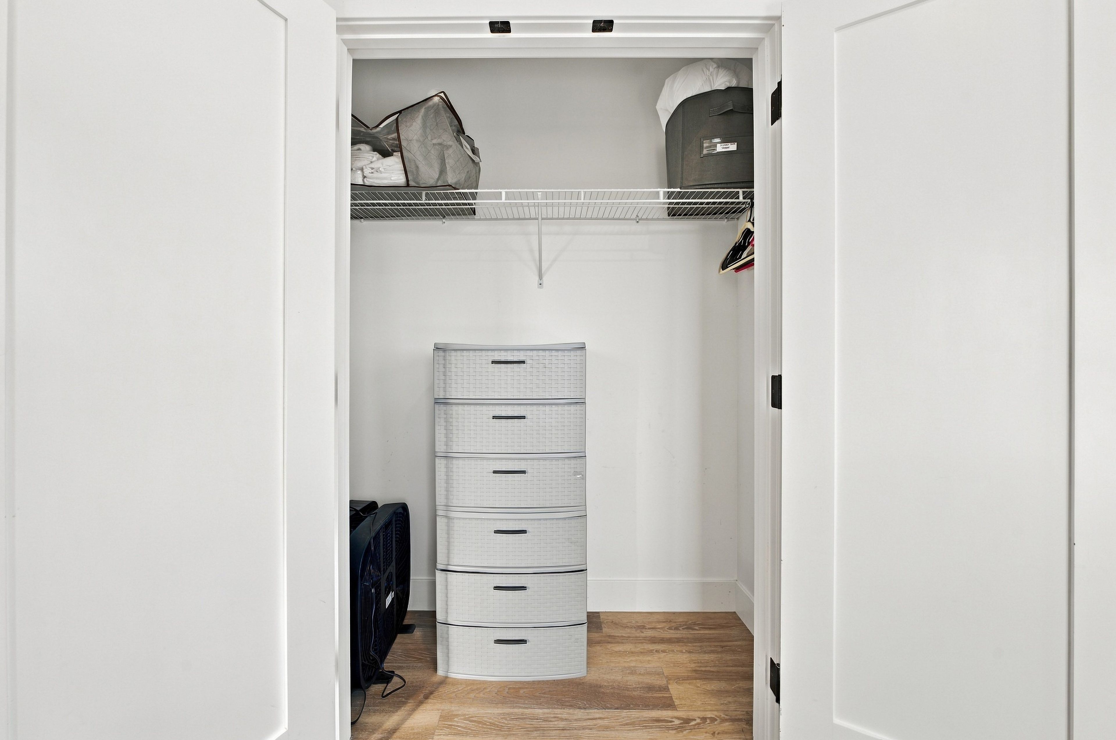 A walk-in closet with a white wardrobe, a hanging shoe rack, and a storage unit with drawers.