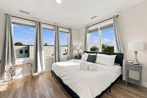 A modern hotel room with a large bed, two bedside tables, a nightstand, a window with curtains, and a view of the outside. - Cityscape Condo: New in Downtown Traverse City! (Traverse City)