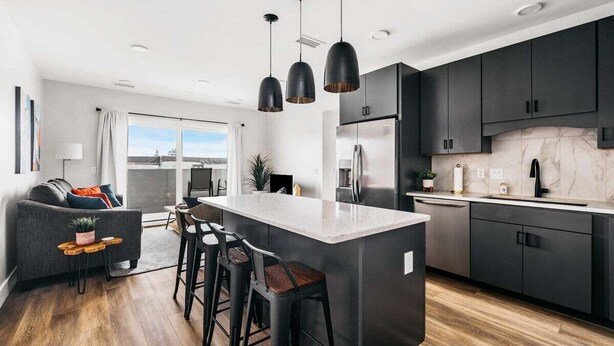 Una cocina moderna con gabinetes oscuros, una isla central con taburetes e iluminación colgante.