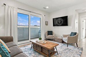 A modern living room with a large sliding glass door, a flat-screen TV mounted on the wall, and a cozy seating area with two armchairs and a sofa. - Cityscape Condo: New in Downtown Traverse City! (Traverse City)