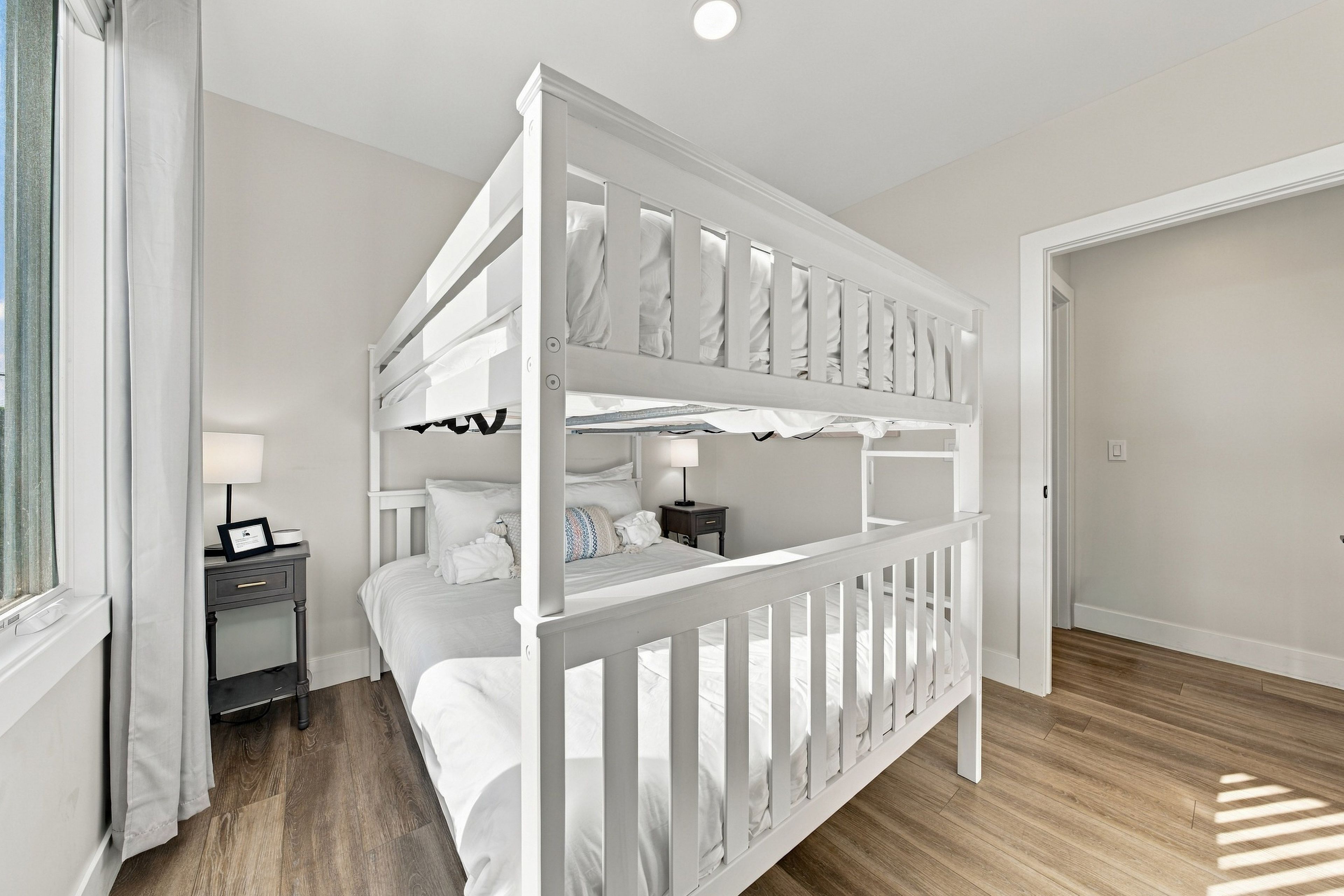 A bunk bed room with a nightstand, a lamp, and a window with curtains.