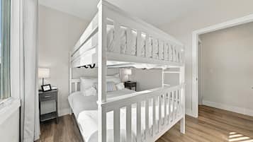 A bunk bed room with a nightstand, a lamp, and a window with curtains.