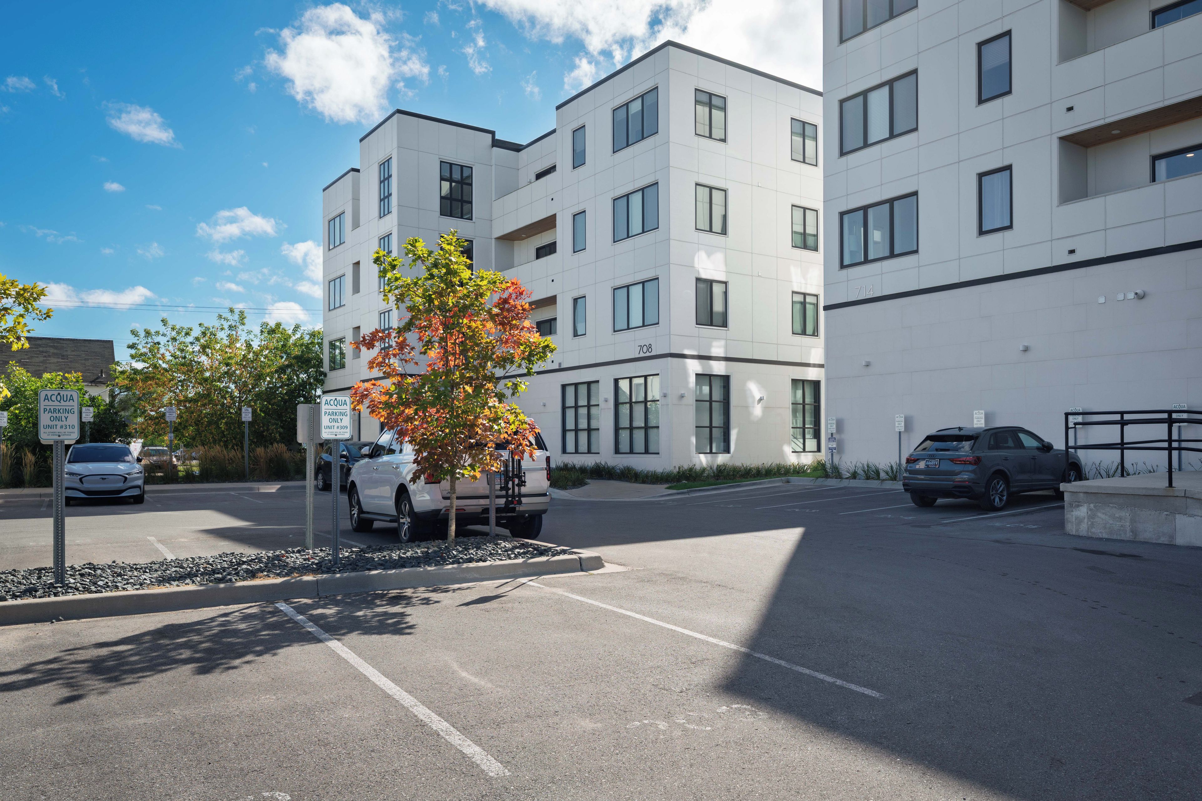 A modern building with multiple floors, parking spaces, and a clear sky.
