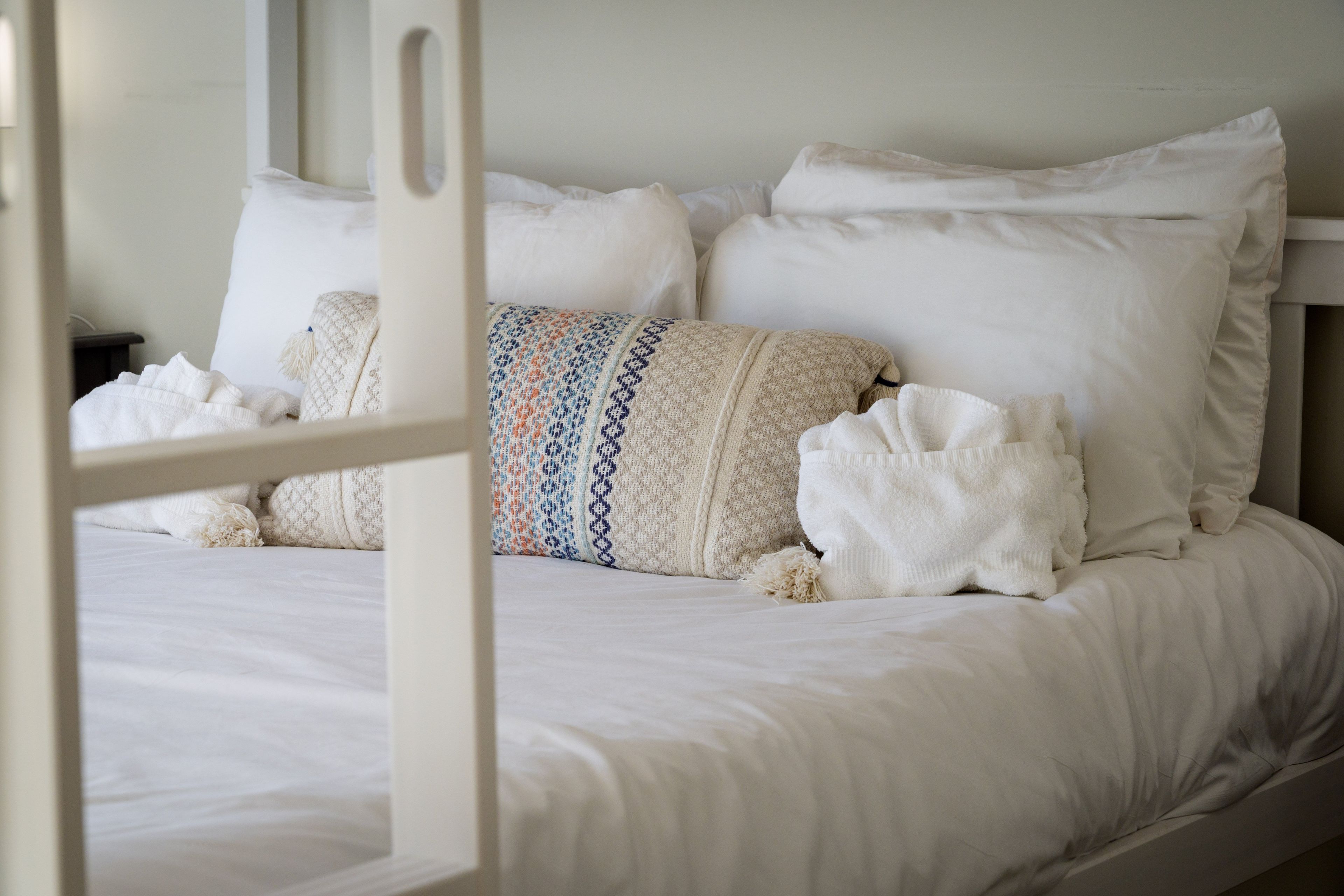 A bed with white linens, a patterned throw pillow, and a white blanket.