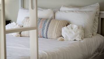 Een bed met witte lakens, een sierkussen met een patroon en een witte deken.