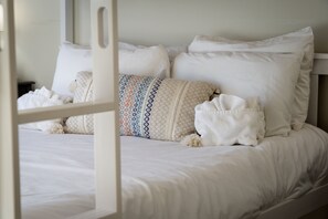 Een bed met witte lakens, een sierkussen met een patroon en een witte deken.