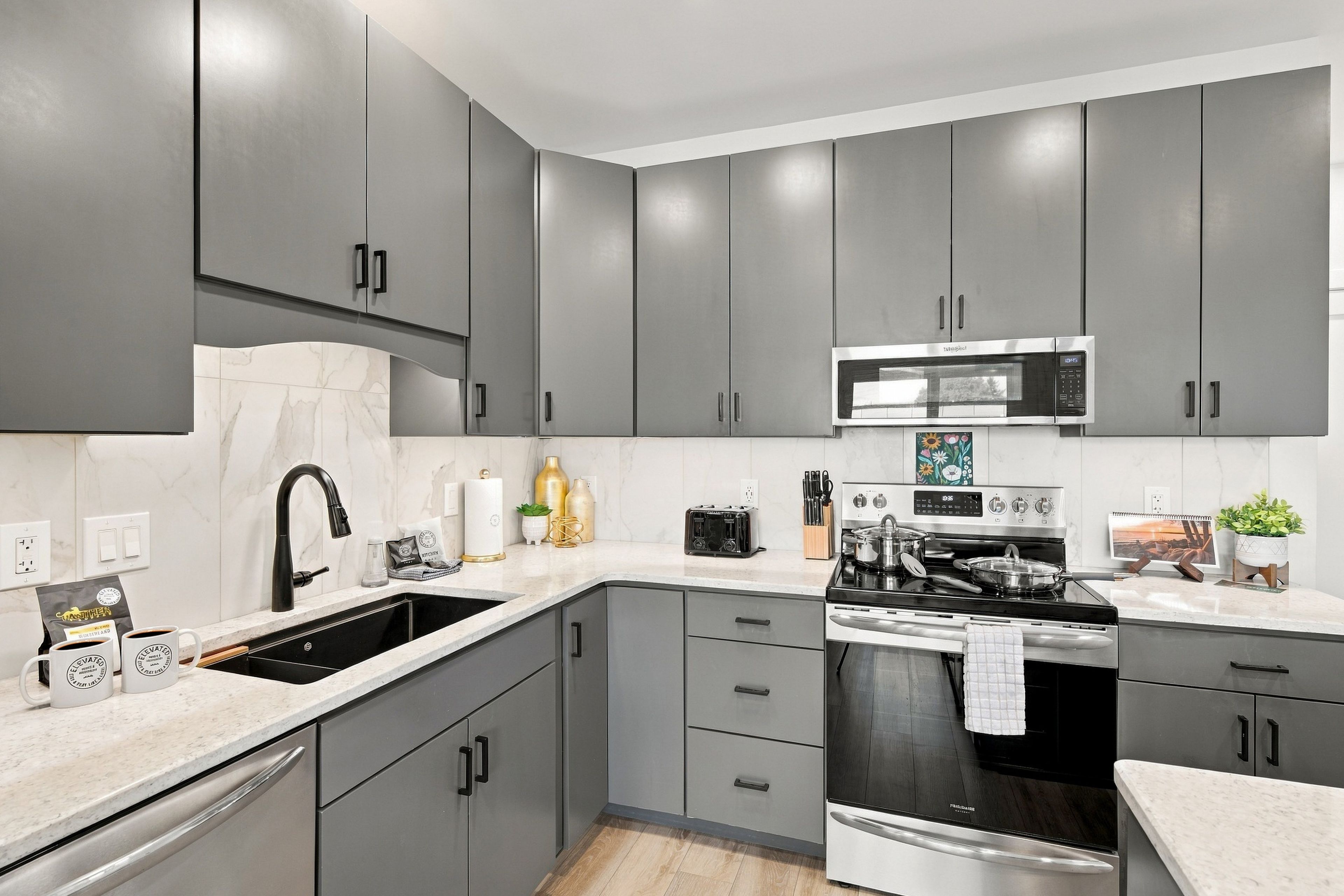 Une cuisine moderne avec des meubles gris, un four à micro-ondes en acier inoxydable, une cuisinière et un évier.