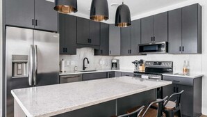 Una cocina moderna con gabinetes oscuros, electrodomésticos de acero inoxidable y una isla grande con taburetes de bar.