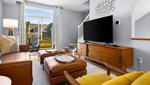 Ein modernes Wohnzimmer mit einer Couch, Poufs, einem Fernseher und einem Holzschrank.