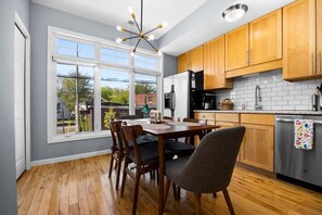 A modern kitchen with wooden cabinets, a stainless steel refrigerator, and a dining area with a wooden table and chairs.