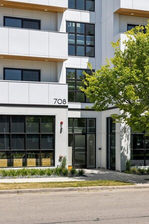 Un bâtiment moderne, avec le numéro 708 sur la façade, de grandes fenêtres et un petit arbre devant.