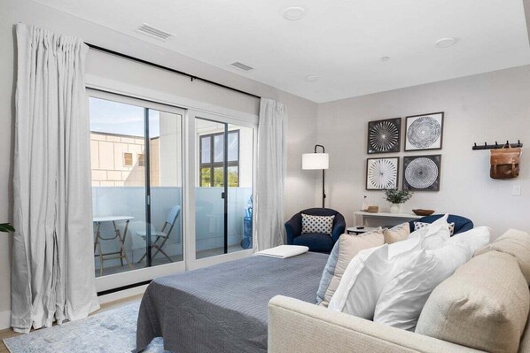 Une chambre moderne comprenant un lit, un canapé, un fauteuil et une grande porte-fenêtre coulissante donnant sur un espace extérieur.
