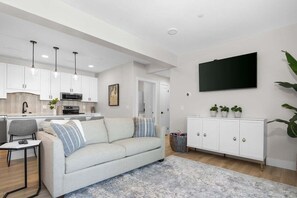 Un salon moderne comprenant un canapé, un coin repas, une cuisine et un téléviseur fixé au mur.