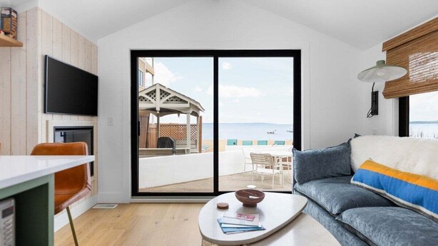 A modern living room with a large sliding glass door leading to a balcony with a view of the sea. - Newly Remodeled Bayview Cabin 6! (Traverse City)