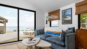 A modern living room with a large sliding glass door leading to a balcony with a view of the sea. - Newly Remodeled Bayview Cabin 6! (Traverse City)