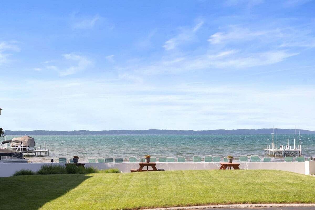 Une vue sur le front de mer, avec une pelouse, deux tables de pique-nique et un quai où est amarré un bateau.