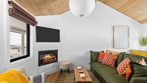 A cozy living room with a fireplace, a green sofa, a wooden coffee table, and a striped rug. - Newly Renovated Beachside Cabin 8! (Traverse City)