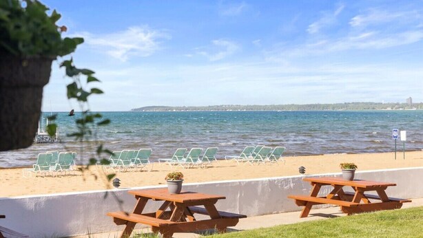 A beachside setting with green lounge chairs and wooden picnic tables, overlooking a calm sea. - Newly Renovated Beachside Cabin 8! (Traverse City)