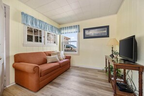 Un salon avec un canapé, un téléviseur et une fenêtre avec des rideaux.