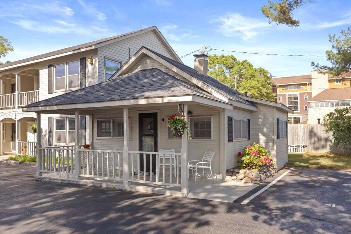 Une maison de plain-pied avec un porche, une cheminée et un petit jardin agrémenté de fleurs et de rochers.