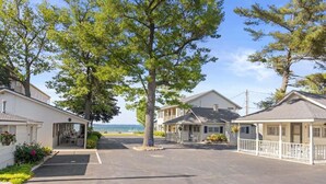 A row of white cabins with a covered parking area, a view of the sea, and a clear sky. - Sandbar Cottage 4 Lakefront 1BR cottage with kitchen, patio, A/C, and parking. (Traverse City)